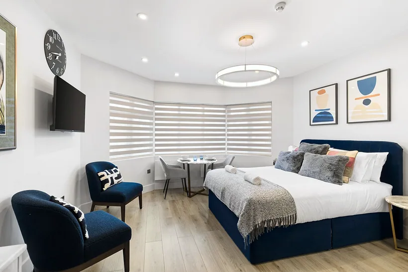 Navy bed and accent chairs in bright bay-window studio, Airbnb photography London