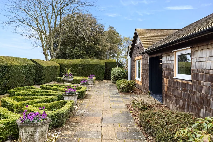Formal knot garden beside timber-clad cottage, blue sky, Airbnb photography London