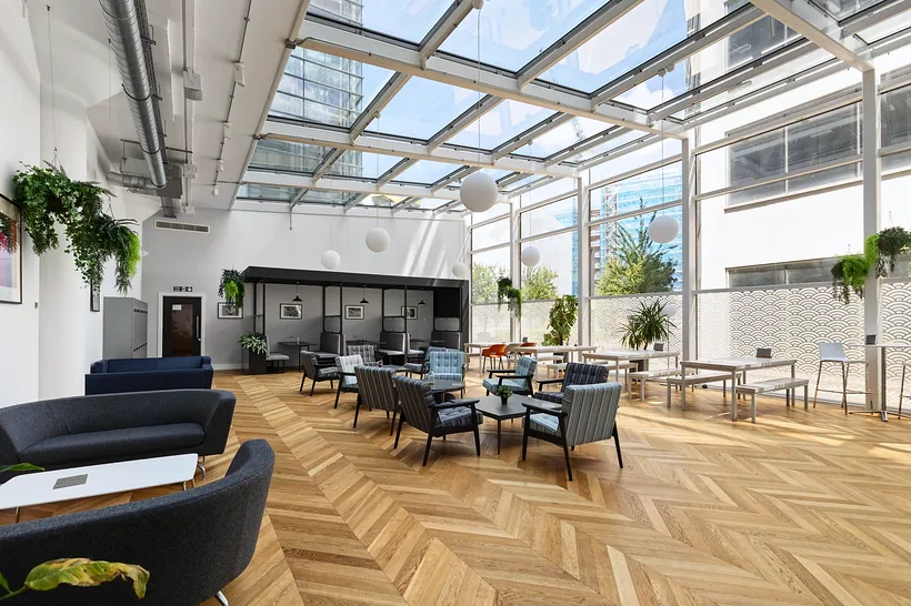 Glass-roofed office lounge with a herringbone floor and hanging plants, commercial photography London