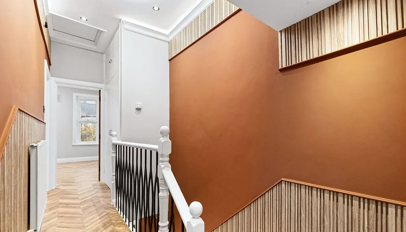 HMO refurb stairwell: burnt-orange wall and slatted timber, developer photography London