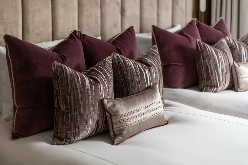 Plum velvet cushions on a panelled-headboard bed, interior photography London