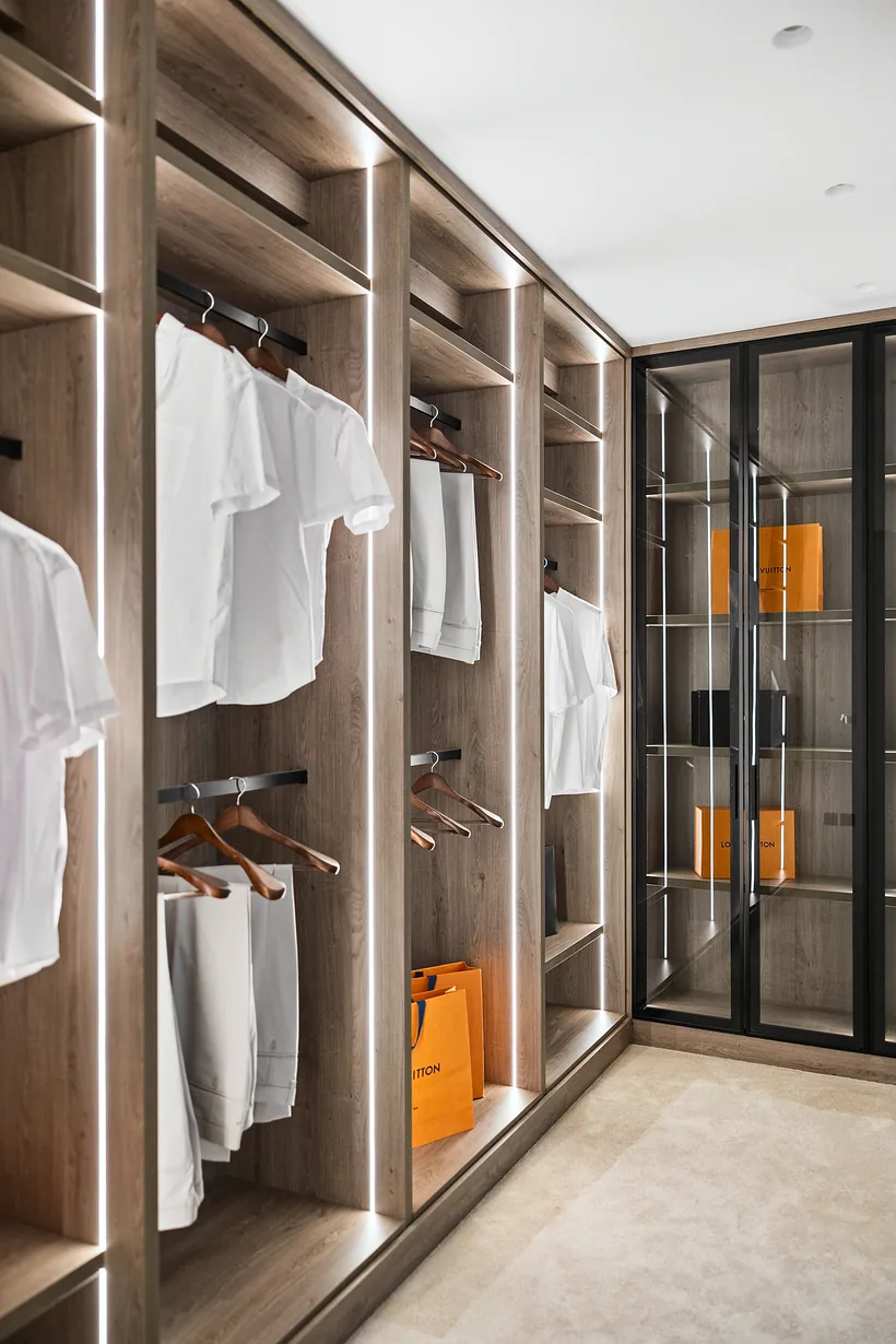 Lit walk-in wardrobe with walnut shelving and glass doors, interior photography London