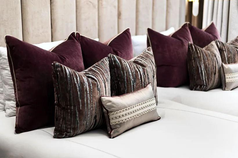 Plum and gold velvet cushion detail on panelled headboard, interior photography London