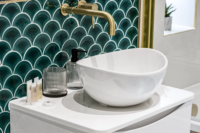 Basin against green fish-scale tiles with a brass tap, interior photography London