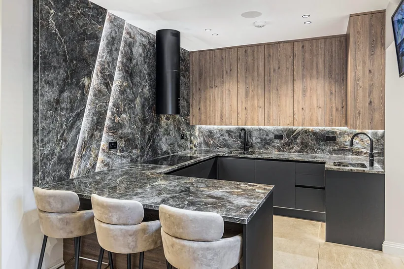Backlit book-matched granite wall with boucle stools, kitchen photography London