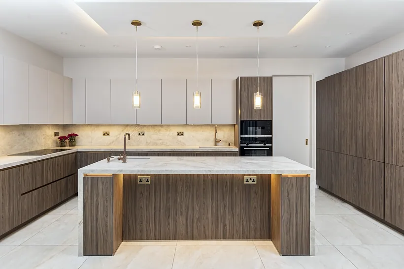 Walnut island with a lit plinth and brass pendants, kitchen photography London